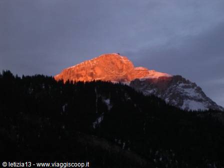 Rocky peak glowing pink in first sunlight above dark forest