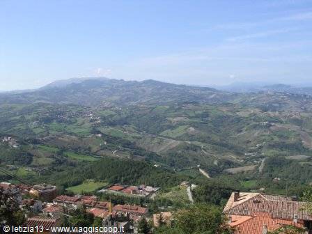 Red tiled rooftops above green cultivated hills under a clear blue sky