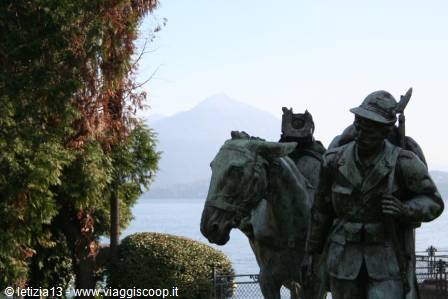 Bronze monument of alpine soldier with mule by the lake, snowy mountains behind