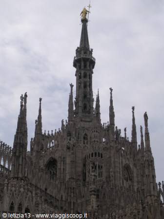 Marble spires of Milan Cathedral with the golden Madonnina against cloudy sky