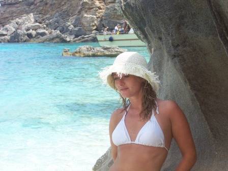 Woman in straw hat and white bikini beside a rock, turquoise water behind