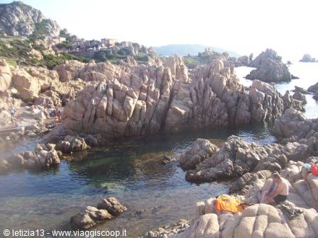 Bathers on pink granite rocks at Costa Paradiso, clear water and stone houses