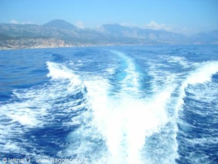 White wake of a boat on blue sea facing Sardinian mountains