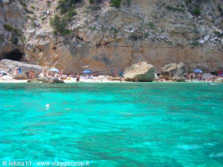 Bathers on the beach beneath a rocky cliff, turquoise water and boulders