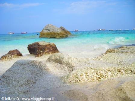 Granite rocks on white sand beach, turquoise sea with anchored boats