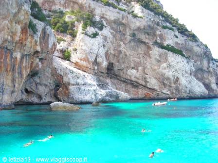 Swimmers in turquoise water beneath limestone cliffs, anchored dinghy, Gulf of Orosei