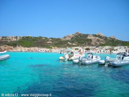 Inflatable boats moored in turquoise water, bathers on the white sand beach