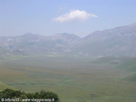 Green plateau of Castelluccio di Norcia surrounded by hazy mountains, blue sky with cloud