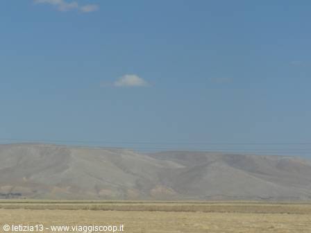 Arid gray mountains beyond a sandy plain under blue sky