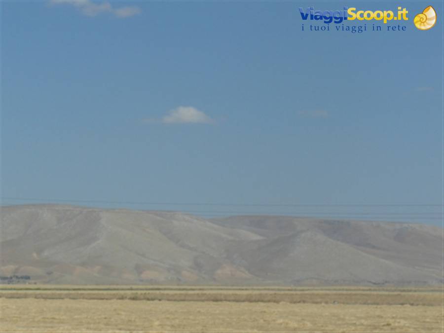 Arid gray mountains beyond a sandy plain under blue sky