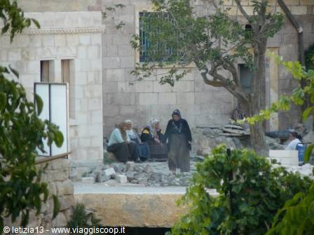 Women sitting outside stone houses, a tree shades the courtyard