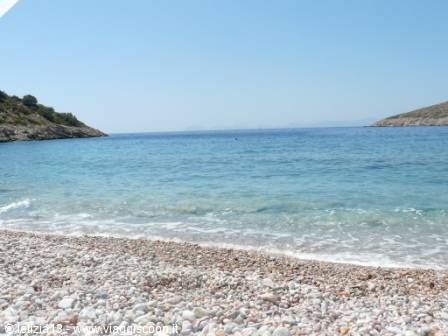 White pebble beach with calm turquoise sea between two rocky headlands