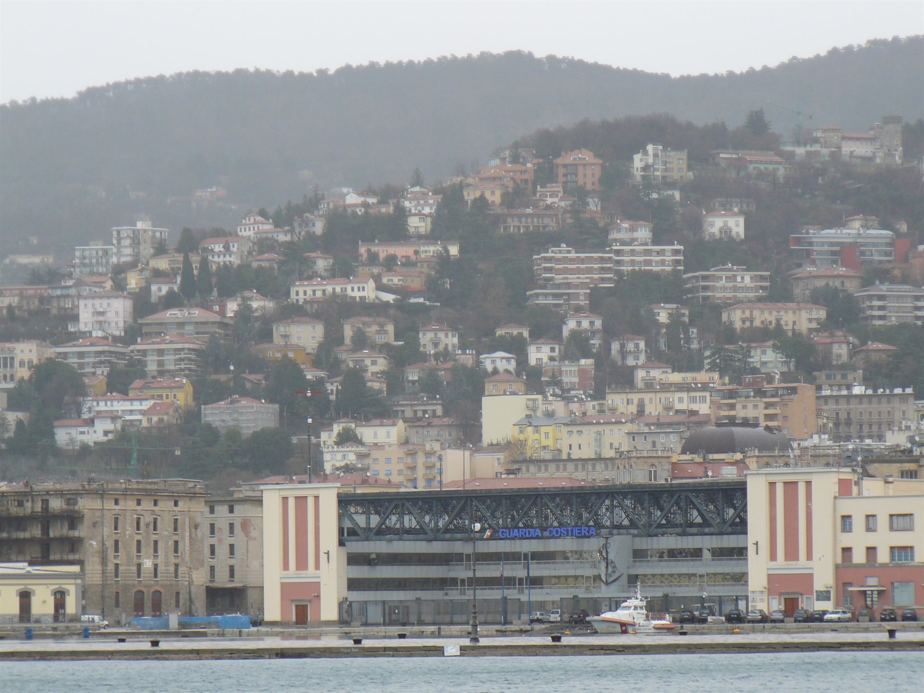 Stazione marittima di Trieste con imbarcazione al molo, case sulla collina retrostante
