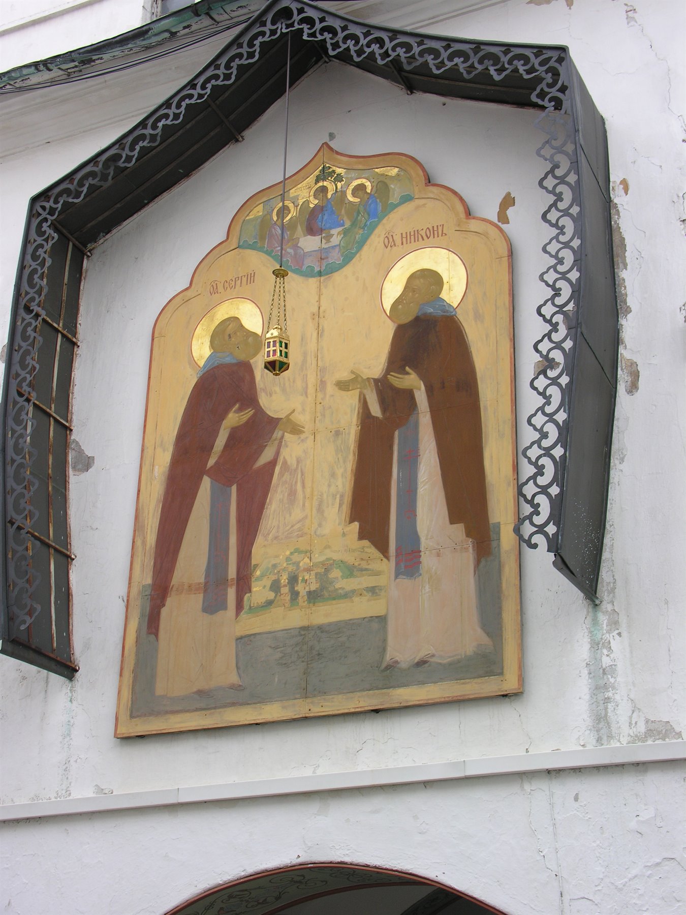Affresco con due santi sotto un baldacchino in ferro battuto su facciata bianca