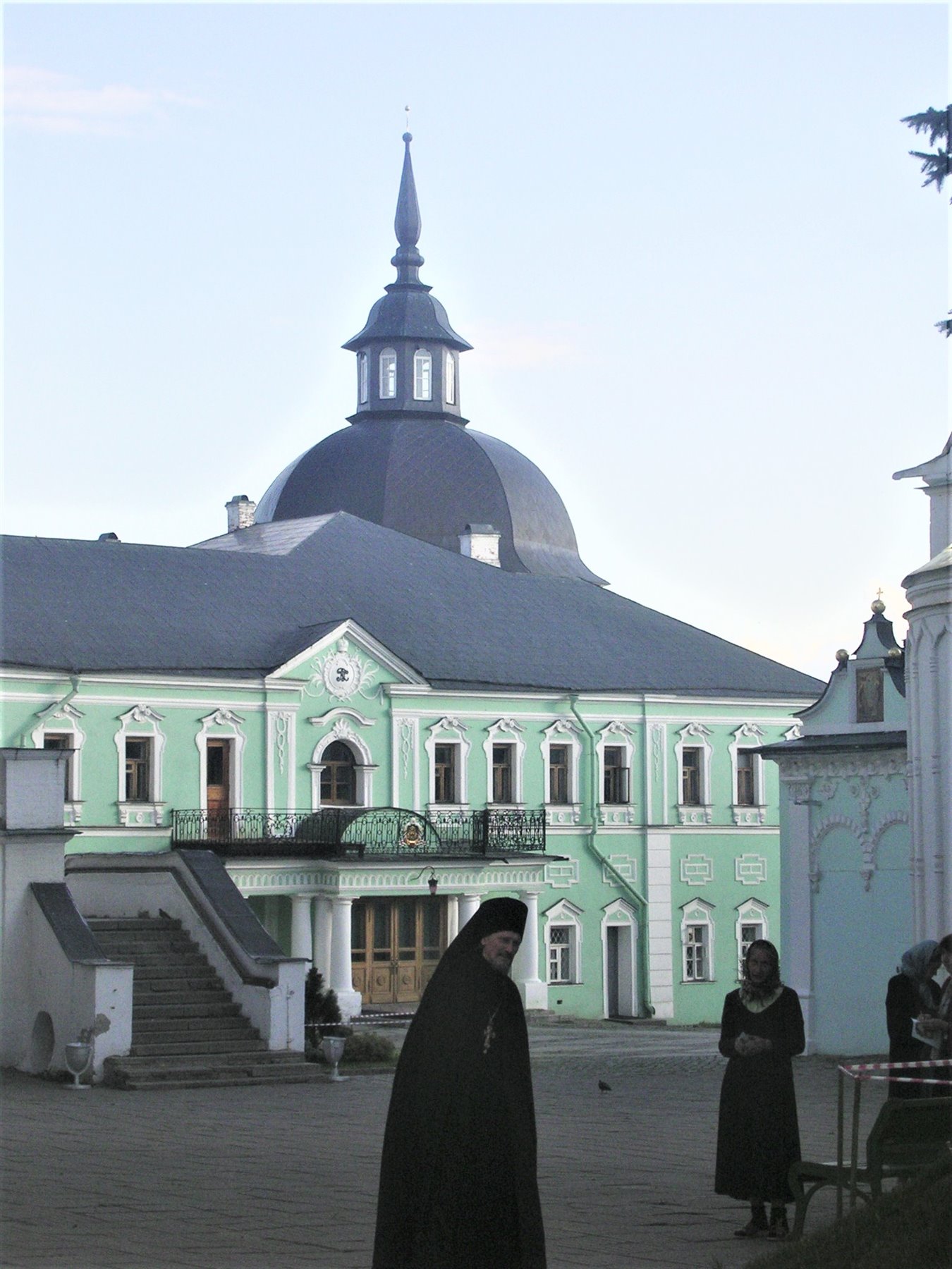 Monache in nero camminano nel cortile di un monastero con edificio verde e cupola