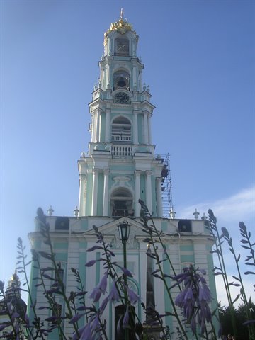 Pale blue baroque bell tower in Sergiev Posad, golden dome, purple flowers in foreground