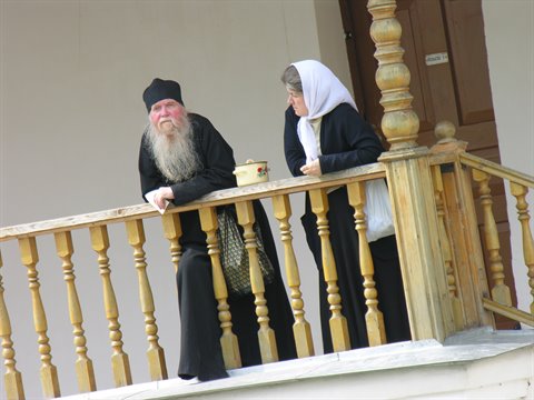 Orthodox monk and nun talking on a wooden monastery balcony
