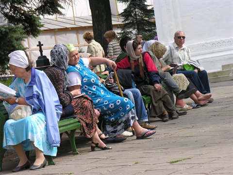 Elderly women in headscarves sitting on green benches in monastery courtyard