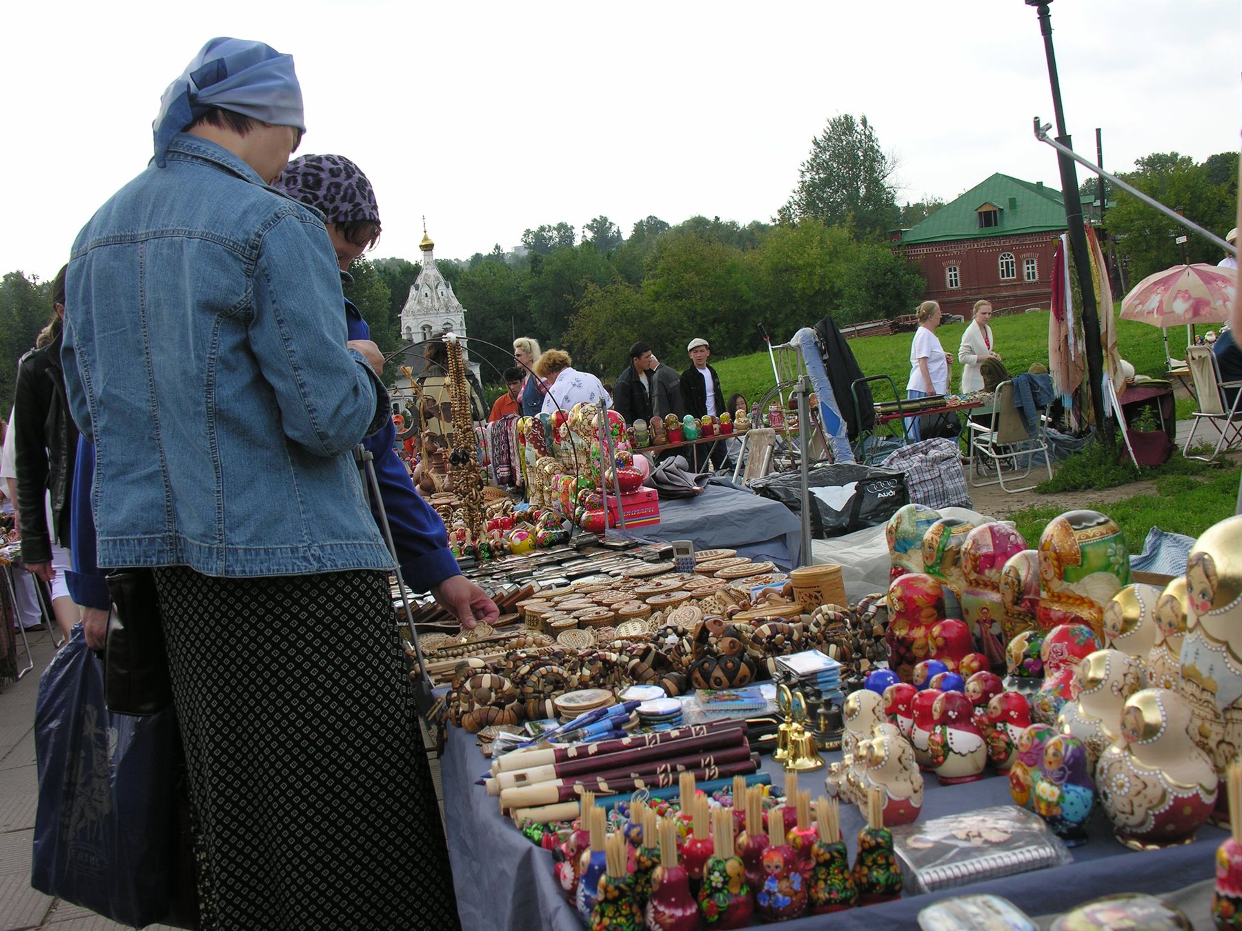 Donna con fazzoletto azzurro osserva matrioske e artigianato in legno al mercatino di Suzdal