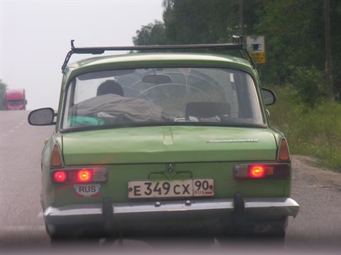 Green Russian car stopped on country road, brake lights on, plate E349CX