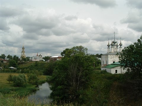 White churches with onion domes beside a stream under grey clouds