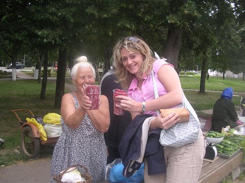 Two smiling women holding cups of red berries at an outdoor market