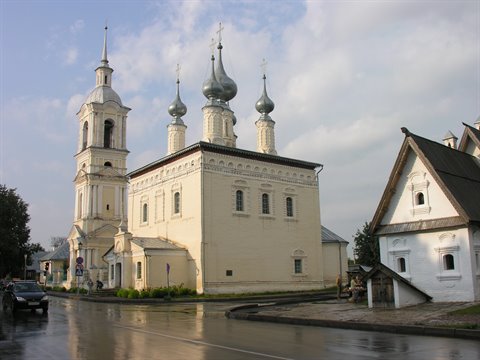 White church with silver onion domes and bell tower on wet street, Suzdal