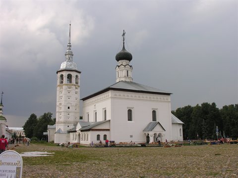 White church with dark dome and bell tower in Suzdal under cloudy sky