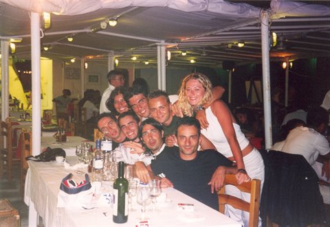 Group of friends posing at table under white tent, bottles and glasses
