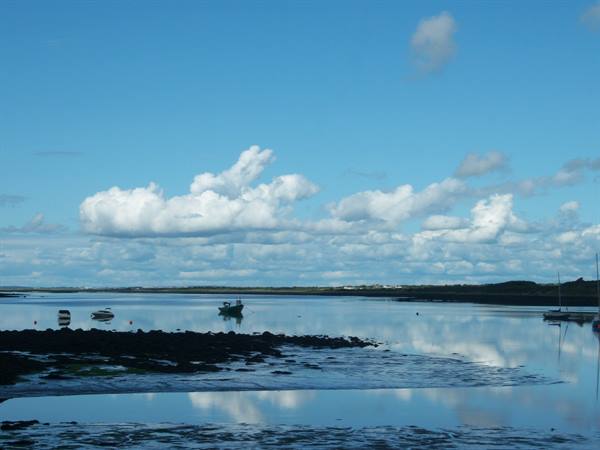 Boats on shallow water with exposed seaweed, clouds mirrored in the tide