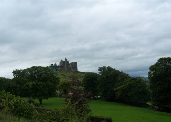 The Rock of Cashel, medieval ruins above green meadow under cloudy sky