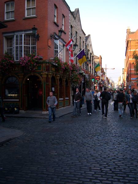 People stroll on cobblestones past a red-brick flowered pub in Dublin