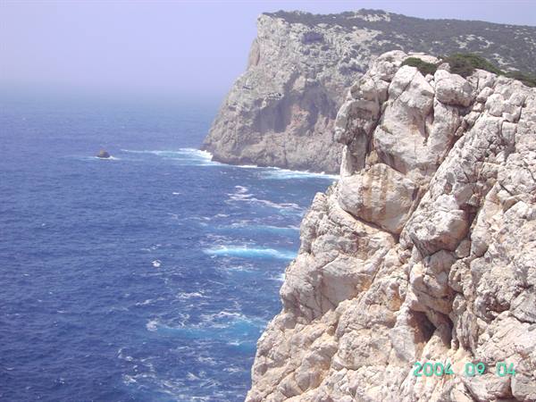 White limestone cliffs plunging into deep blue sea, foam among rocks