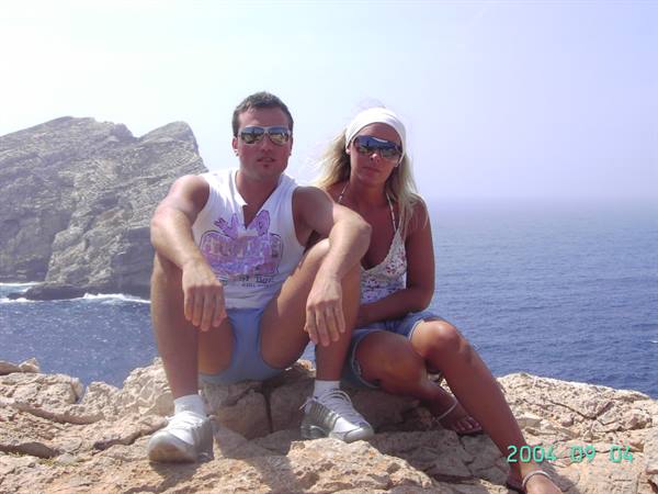 Couple in sunglasses sitting on limestone rock above blue sea