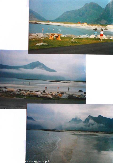 Tourists on sandy beach beneath rugged mountains, wooden picnic table on grass, Lofoten