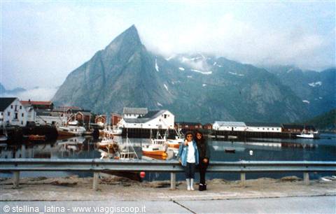 Two girls by the road at Reine harbor, boats and Lofoten peaks in mist