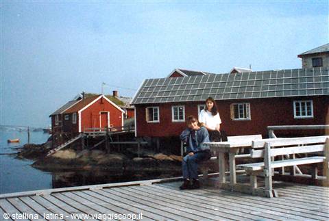 Two women on a wooden bench by red stilt fishing cabins in Lofoten