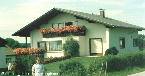 Tyrolean house with wood balcony and red flowers, woman on lawn
