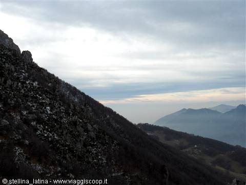 Mountain slope with rocks and shrubs under heavy clouds, misty distant peaks