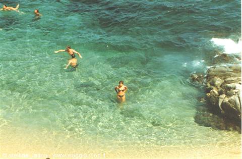 Swimmers in clear turquoise water near rocks, golden sandy beach