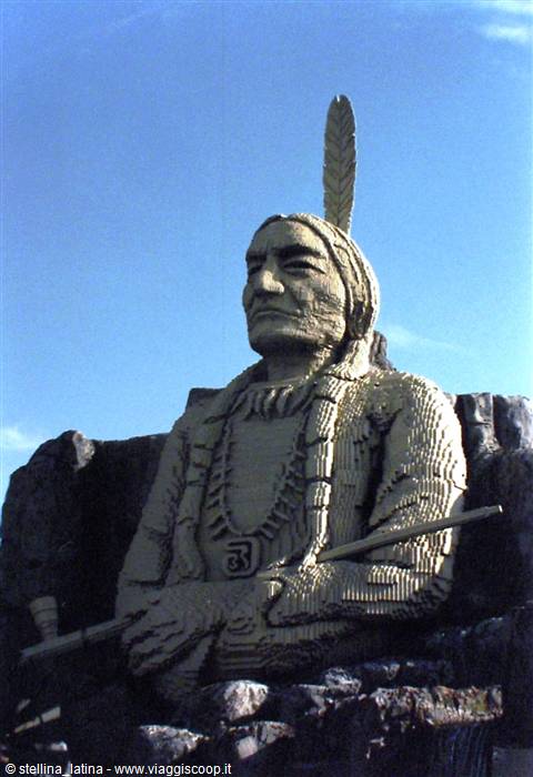 Stone statue of Native American chief with feather and peace pipe against blue sky