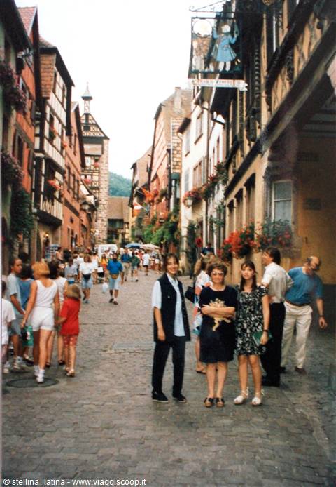 Smiling tourists on cobbled street among half-timbered houses in Riquewihr
