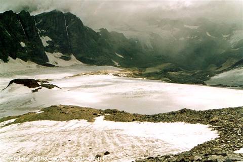 Glacier below rocky peaks under clouds, snow and scree in foreground