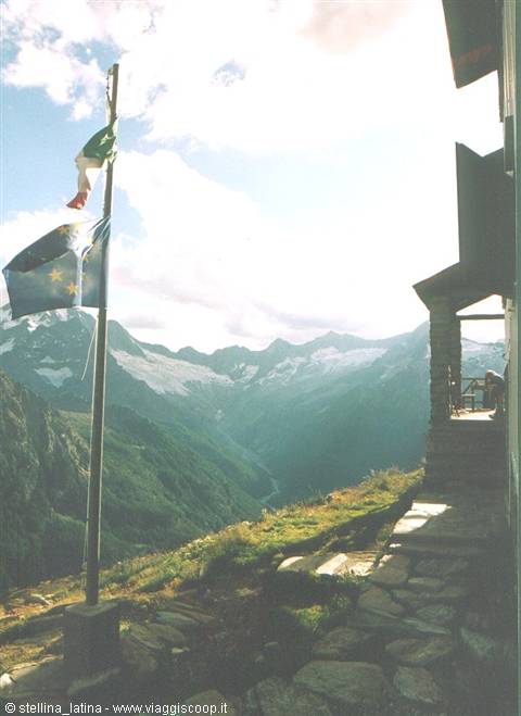 Italian and European flags waving in front of a stone mountain hut