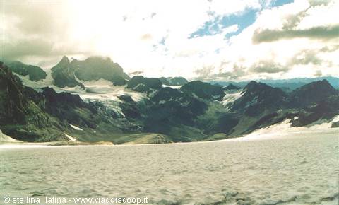 Glacier in the foreground, rocky snowy peaks under a cloudy sky