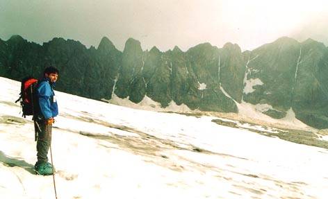 Mountaineer with red backpack and pole on snow before jagged rock spires
