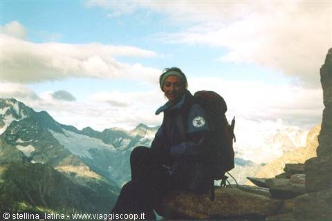 Hiker with backpack sitting on rock among snowy peaks and clouds
