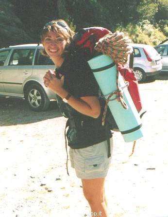Smiling woman with hiking backpack and sleeping mat, parking lot among cars
