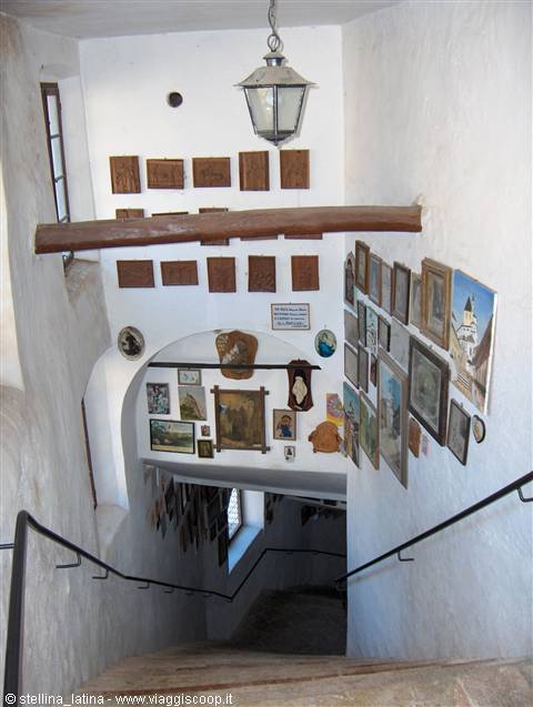 White staircase walls covered with paintings, hanging lantern and wooden beam