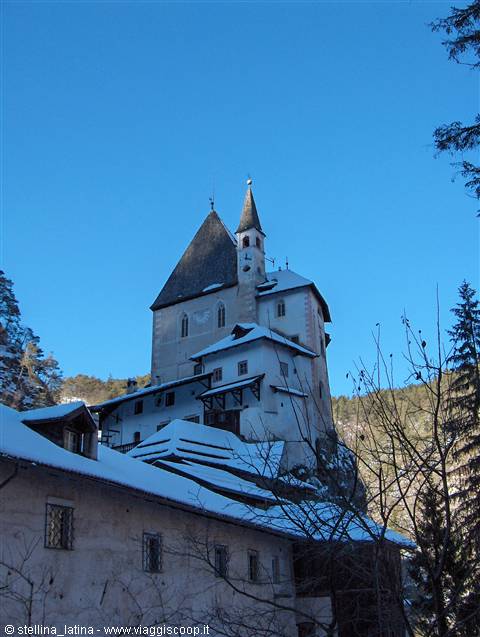 San Romedio sanctuary, white snow-covered building on rock among firs, blue sky